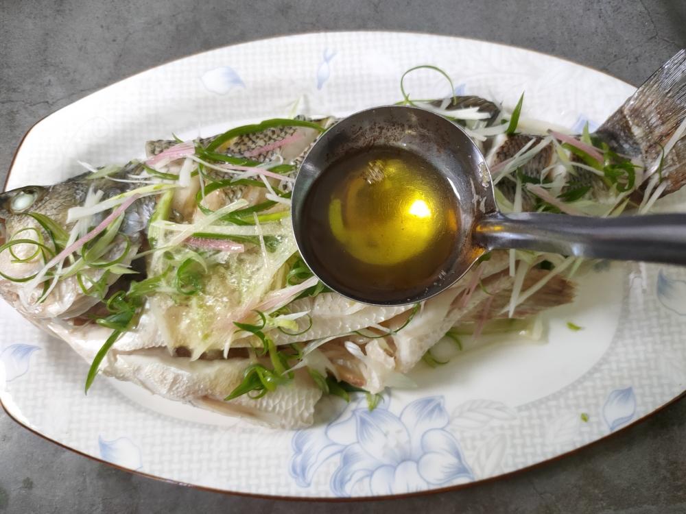 Drizzling seasoned soy sauce over the steamed sea bass
