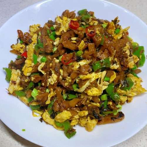 Waipocai chao dan - grandma's pickled greens stir-fried with soft eggs, chilies, and garlic scapes in a wok