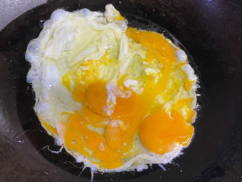 Soft egg curds being pushed around in hot oil in the wok, still glossy and barely set
