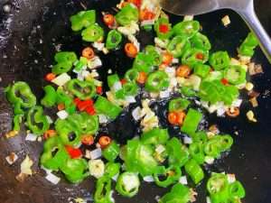 Chopped chilies dry-frying in the wok, skins blistering and charring at the edges