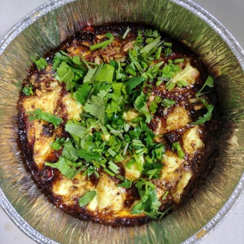 Air fryer foil tofu in a foil container topped with sizzling garlic chili sauce and fresh cilantro