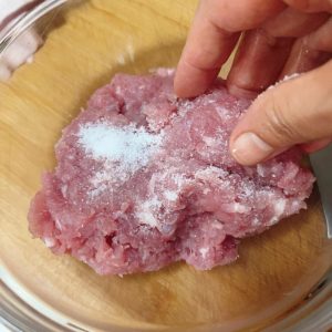 Hand-formed lean pork meatballs in a bowl after being thrown to develop stickiness