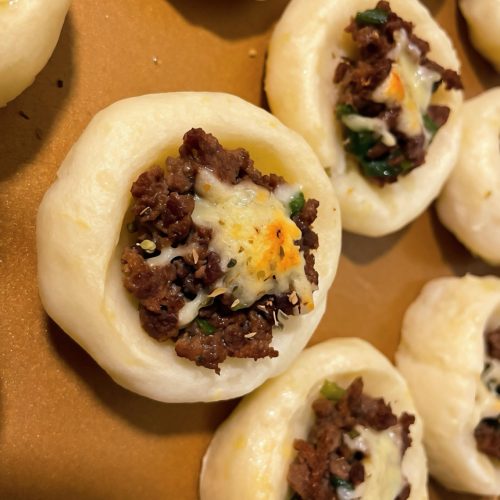 Beef and cheese potato tarts on a baking sheet with melted mozzarella and minced beef filling