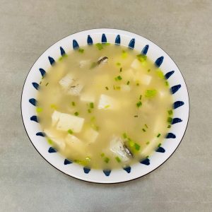 A bowl of Bombay duck and tofu soup with silky tofu cubes, tender fish segments and chopped scallion in a light broth
