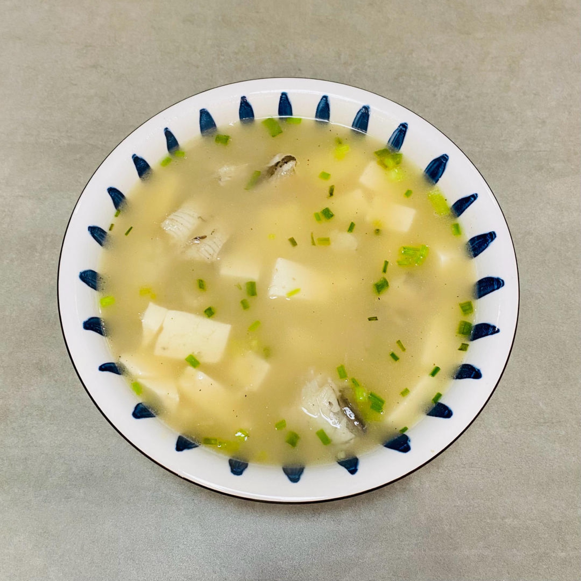 A bowl of Bombay duck and tofu soup with silky tofu cubes, tender fish segments and chopped scallion in a light broth