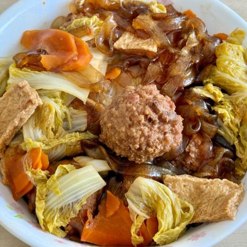 Braised cabbage vermicelli with meatballs in a shallow pot, garnished with scallions