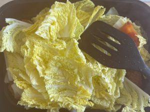 Lay the cabbage leaves on top, add a splash of water to the pot, and continue cooking until they wilt.