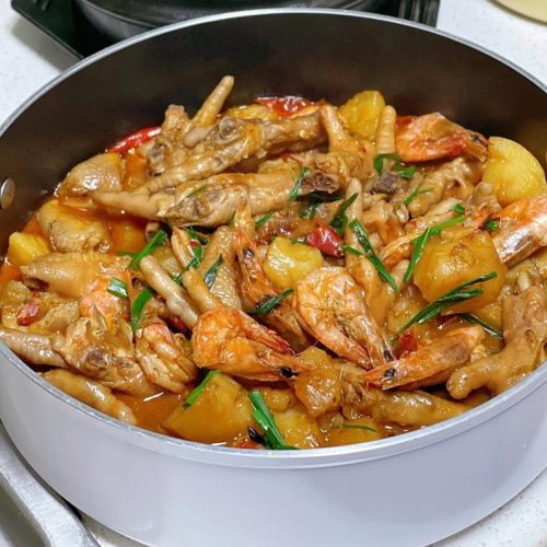 Braised chicken feet and shrimp pot in a wok with potatoes, carrots, and glossy dark sauce