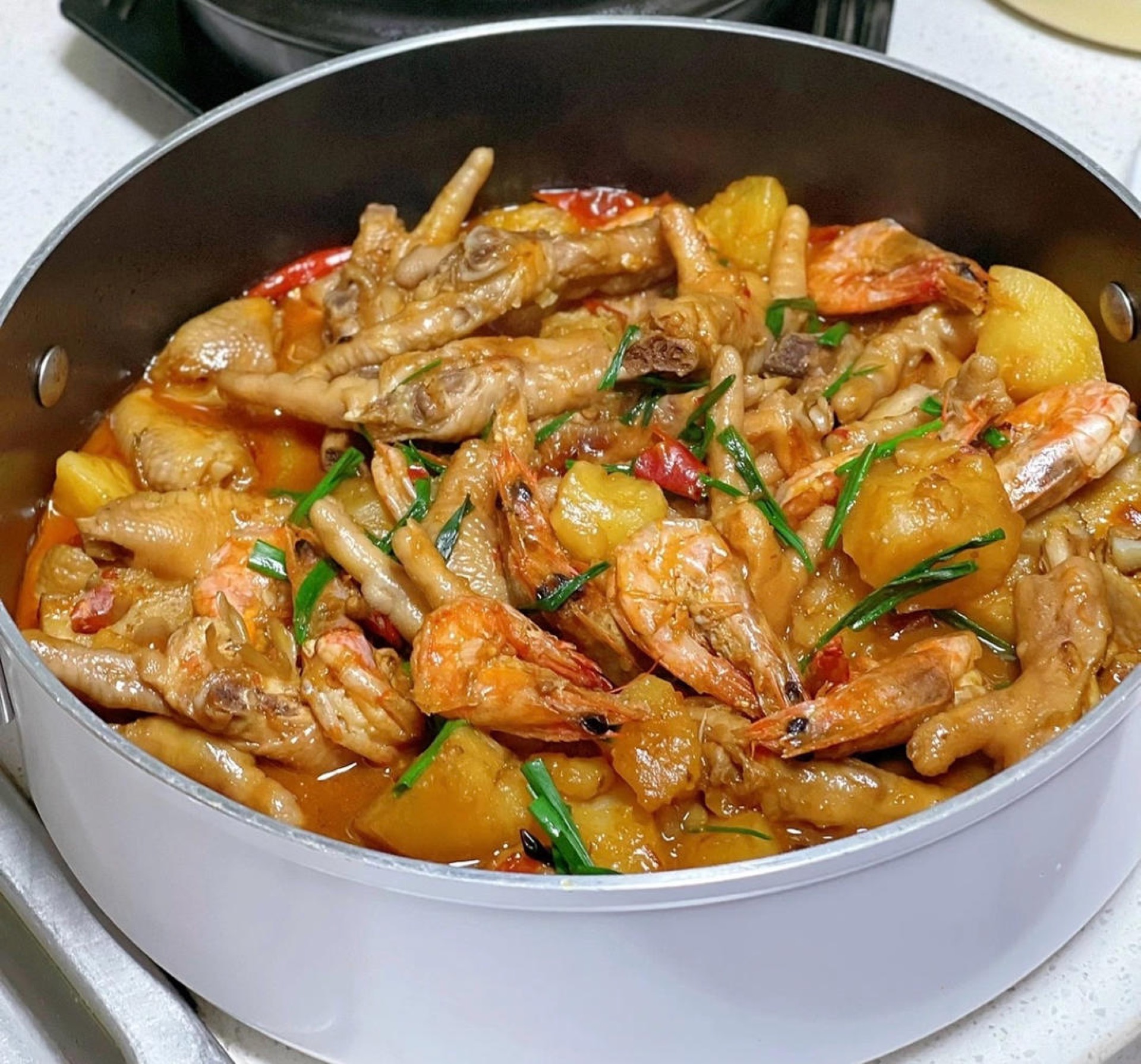 Braised chicken feet and shrimp pot in a wok with potatoes, carrots, and glossy dark sauce
