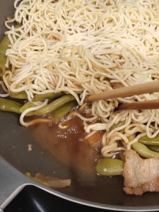 Check the liquid in the wok: tilt it and you should still see some broth, but not too much; now uncover and use chopsticks to lift and toss the green beans and noodles together, an