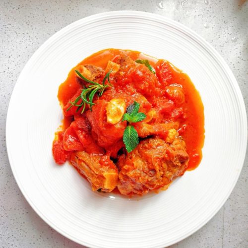 Braised oxtail with tomato in a dark braising pot, garnished with fresh herbs
