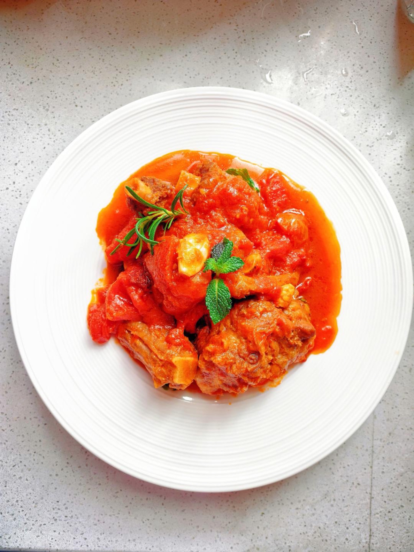 Braised oxtail with tomato in a dark braising pot, garnished with fresh herbs