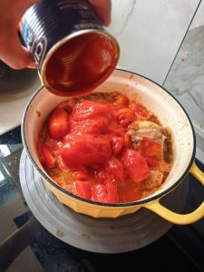 Add one can of canned tomato, the chopped fresh tomatoes, and a little hot water. Braise, or pressure-cook it — bring it up to pressure over high heat, then turn to low.