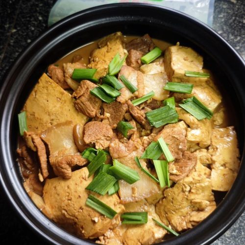 Braised pork with tofu in a clay pot, garnished with garlic sprouts