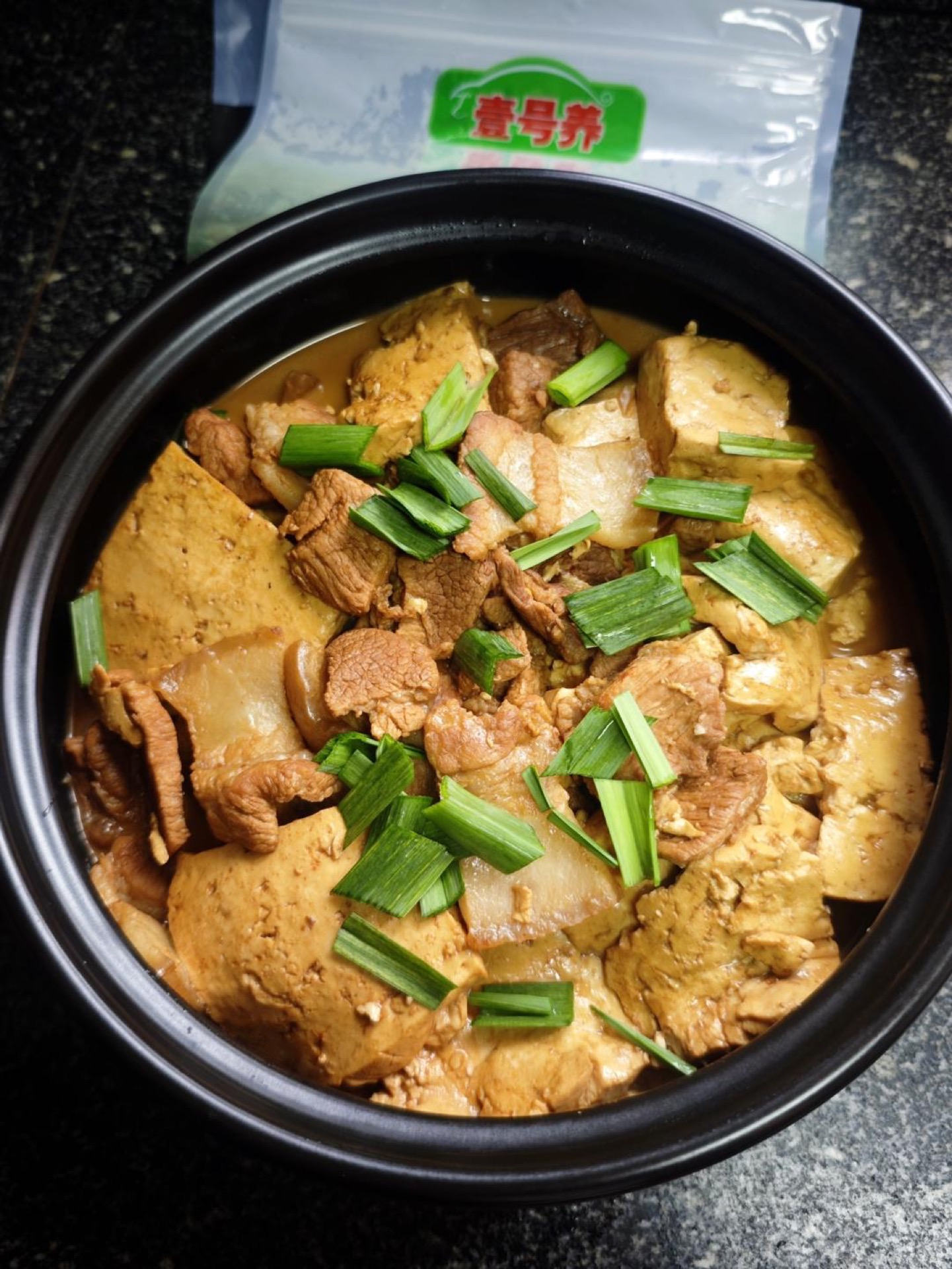 Braised pork with tofu in a clay pot, garnished with garlic sprouts