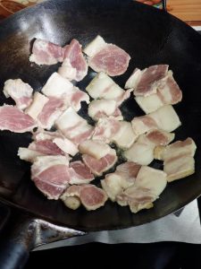 Heat the wok, add a little oil to coat it, then add the fatty pork pieces and sear them until one side is golden before turning to sear the other side.