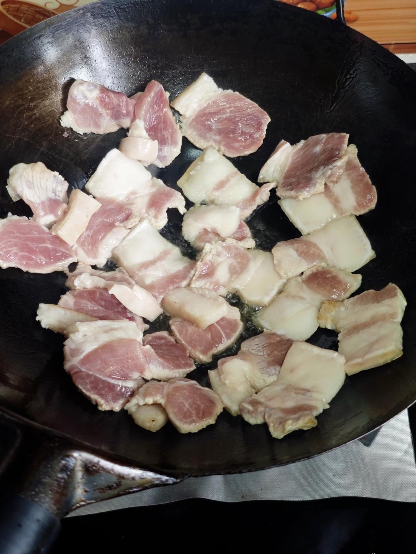 Heat the wok, add a little oil to coat it, then add the fatty pork pieces and sear them until one side is golden before turning to sear the other side.