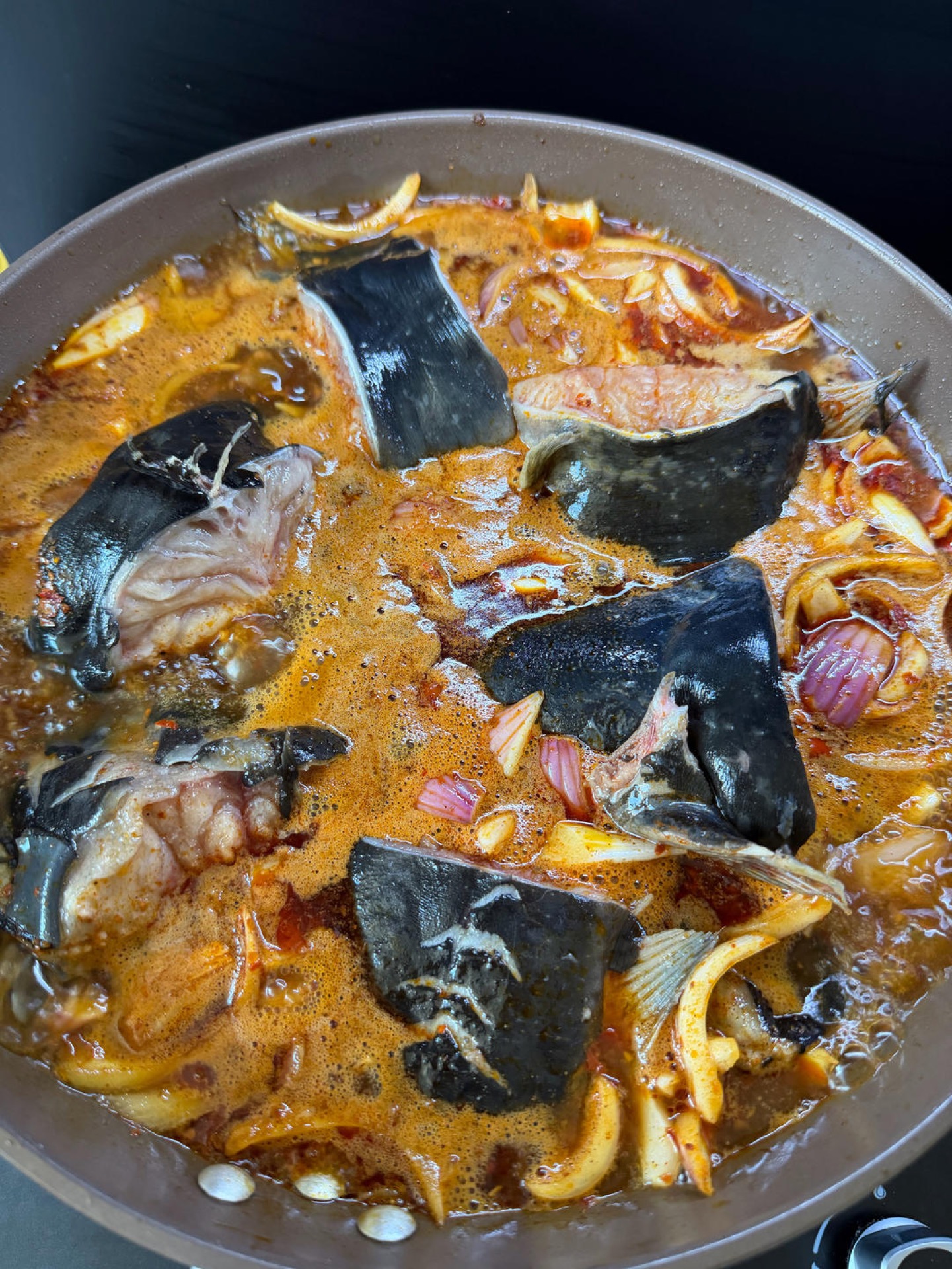 Fish chunks simmering in a shallow pool of red braising liquid