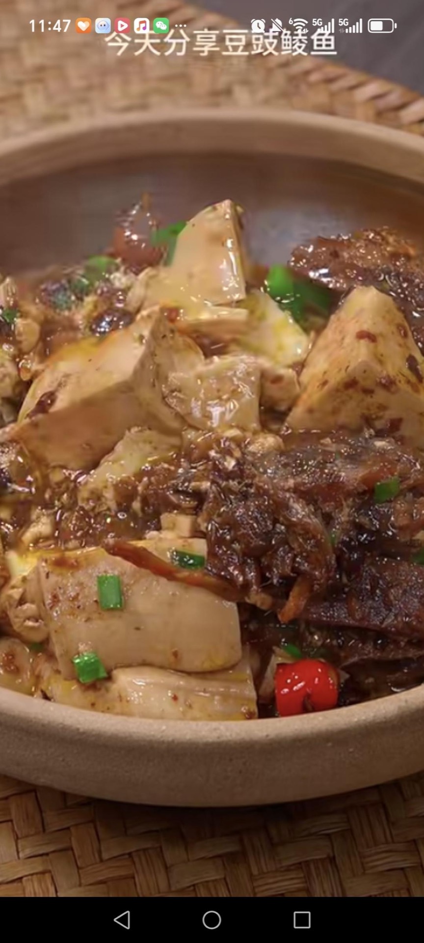 Braised tofu with dace in black bean sauce in a white dish, topped with sliced red chilies and scallions