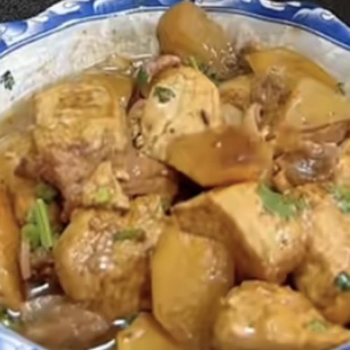 A bowl of braised tofu with potatoes garnished with scallions, green chilies, and cilantro