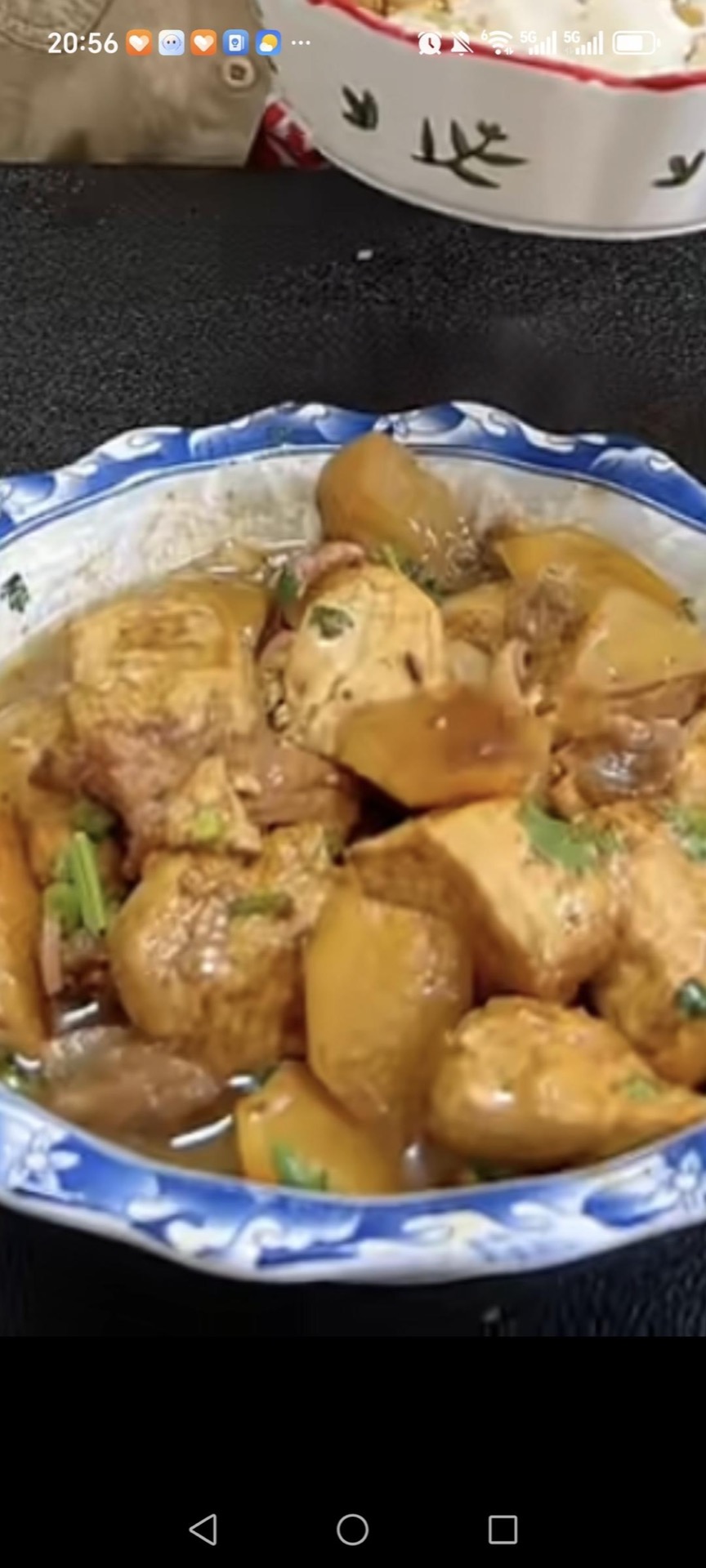 A bowl of braised tofu with potatoes garnished with scallions, green chilies, and cilantro