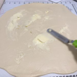 Rolling the dough into a round and spreading butter over it