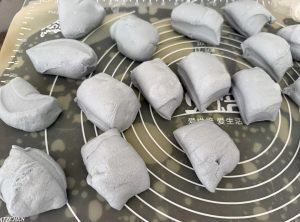 Blue buns filled with cheese being rounded and proofed