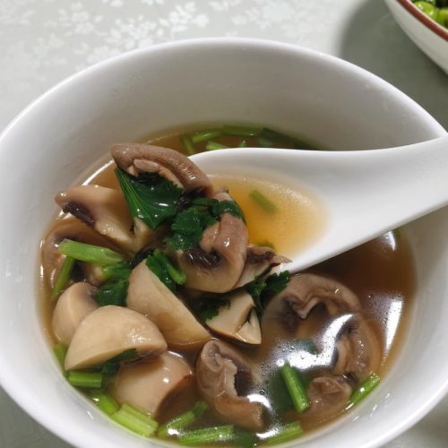 A bowl of clear button mushroom soup garnished with scallions and cilantro