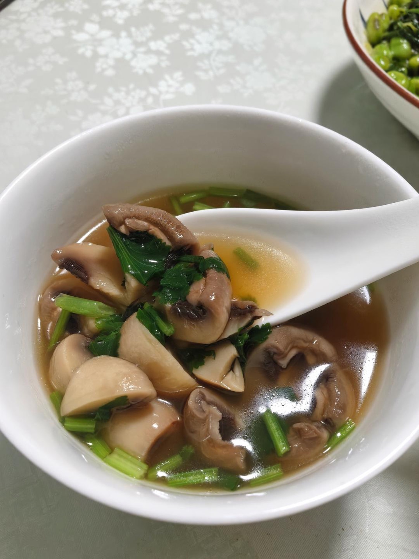 A bowl of clear button mushroom soup garnished with scallions and cilantro