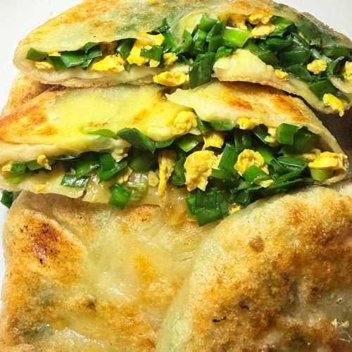 Chive and egg pancakes stacked on a plate with a thin golden skin and green chive filling showing