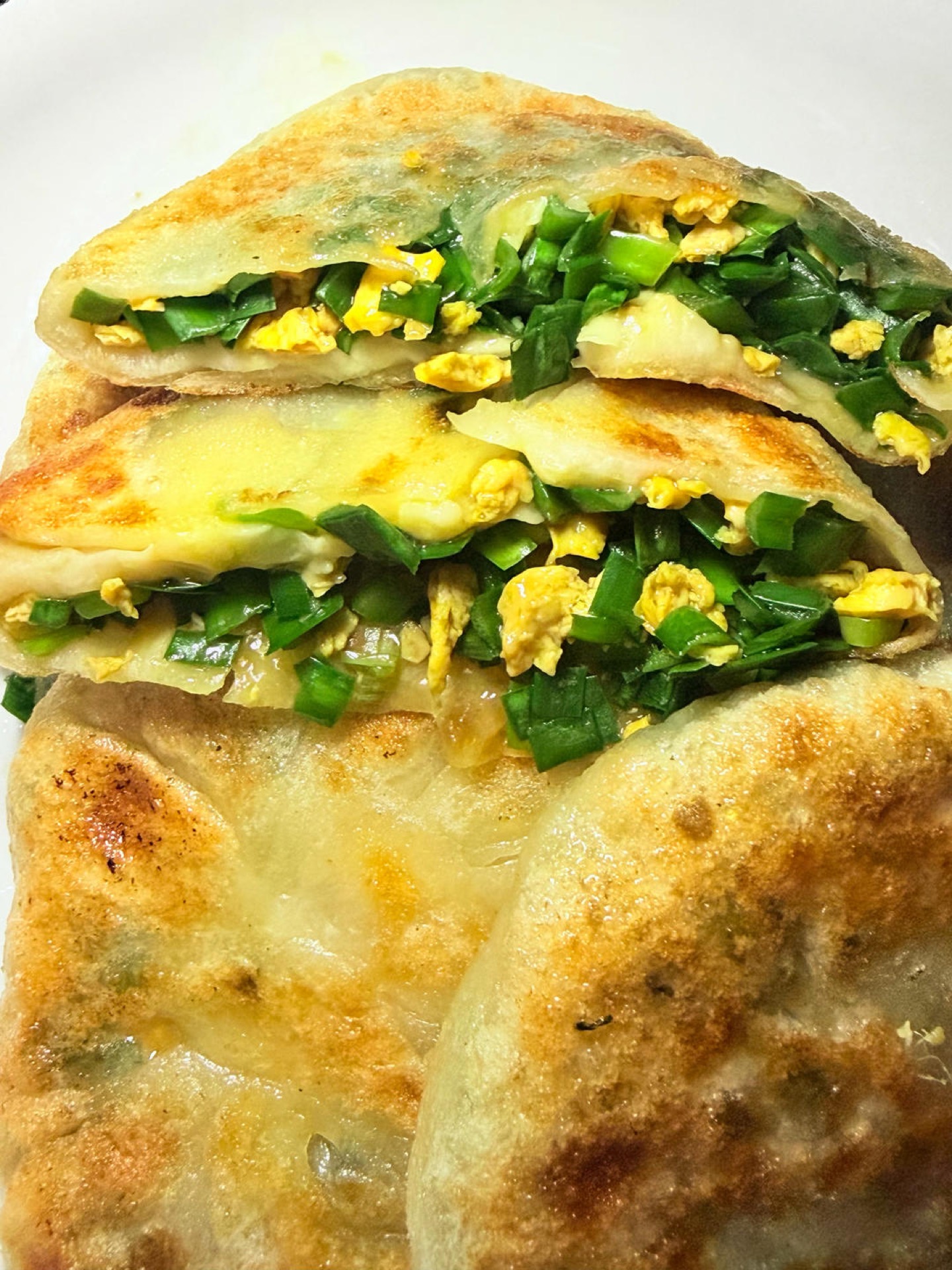 Chive and egg pancakes stacked on a plate with a thin golden skin and green chive filling showing