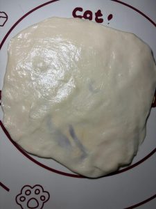 Take one piece of dough onto a mat, put on gloves, and press it flat with your palm, then stretch it into a very thin wrapper; you do not even need a rolling pin because the dough