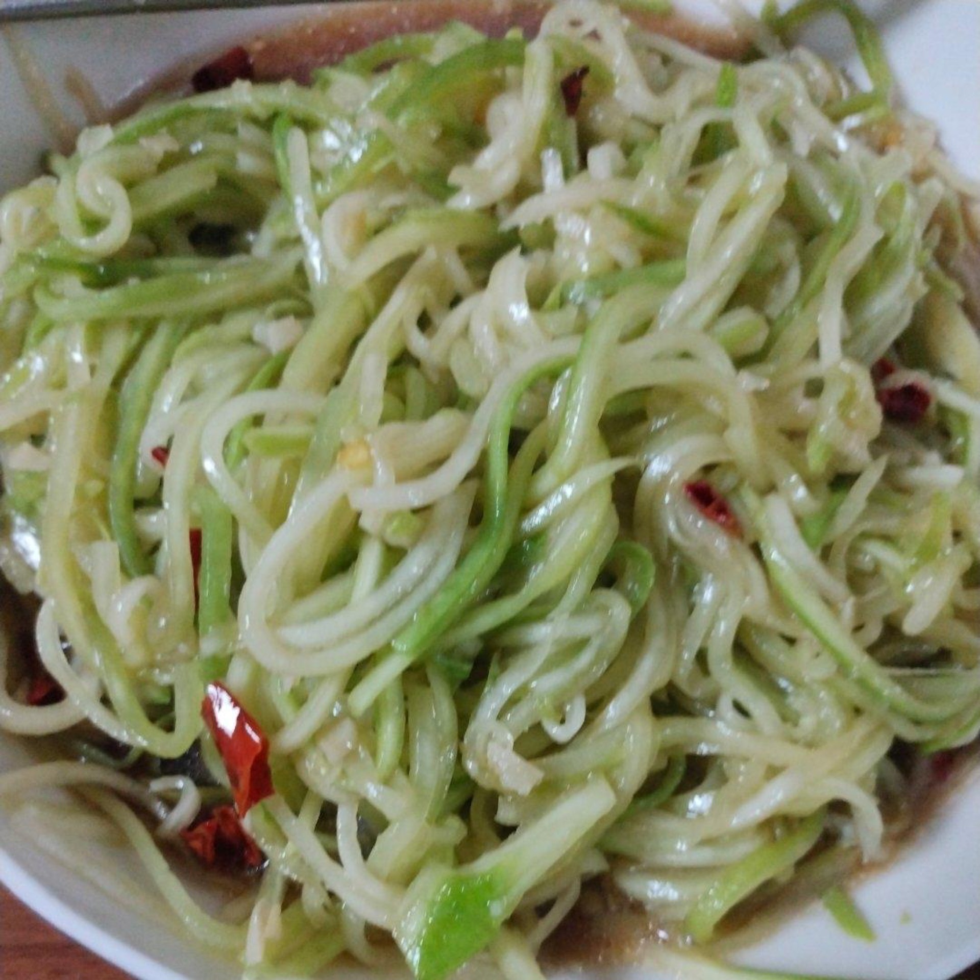Cold tossed gourd salad in a white bowl, garnished with chili and sesame