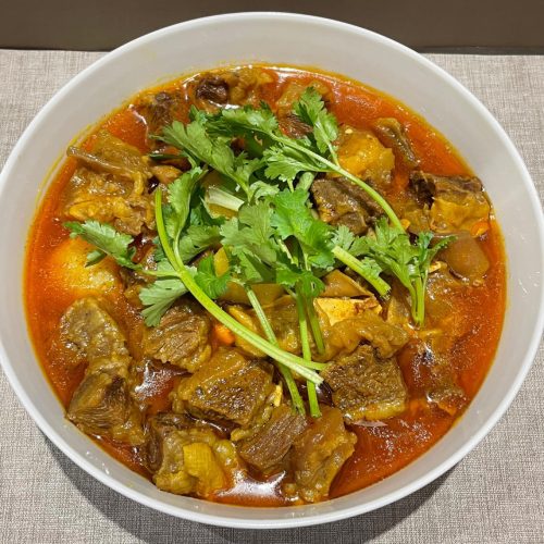 Curry beef brisket with tofu and potato in a dark pot, garnished with scallion
