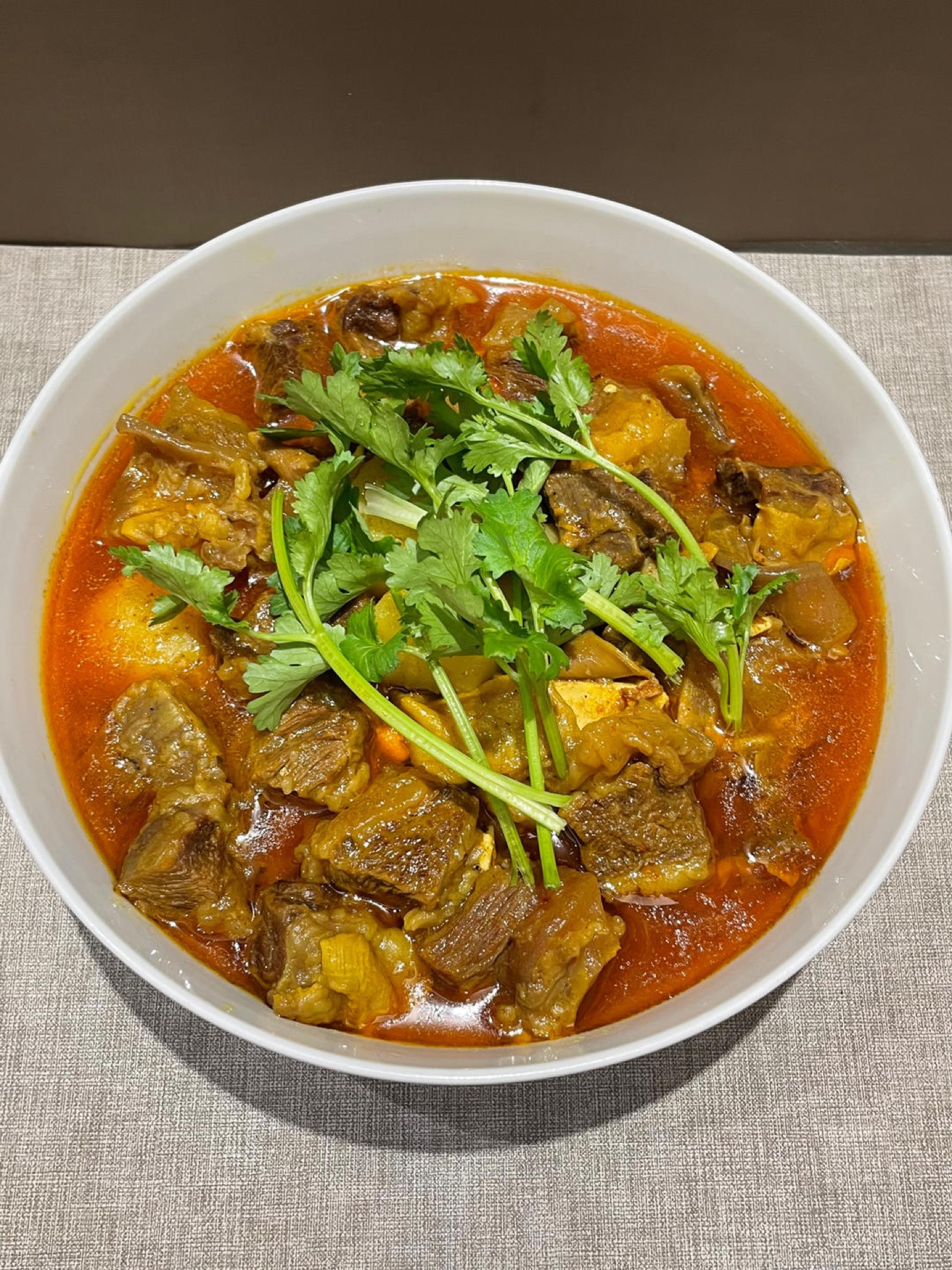 Curry beef brisket with tofu and potato in a dark pot, garnished with scallion