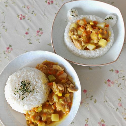 A bowl of curry chicken leg rice with golden curry sauce, chicken cubes, potato and carrot over steamed white rice, garnished with sesame seeds