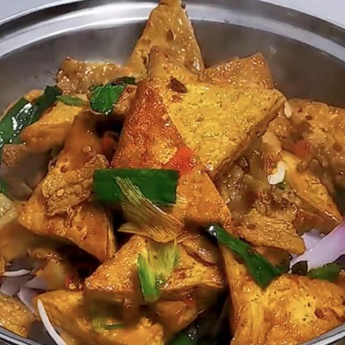 Dry pot tofu with crispy golden tofu triangles and pork belly served over sliced onion in a dry pot