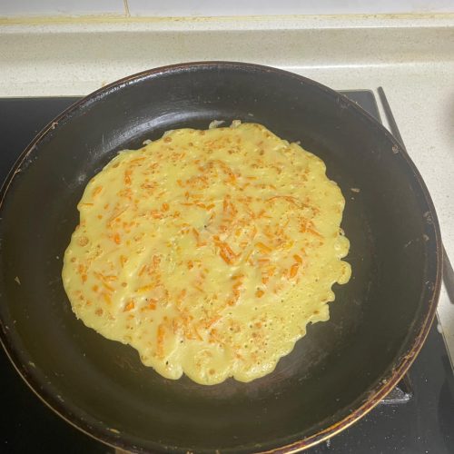 A stack of soft golden egg pancakes with grated carrot on a plate