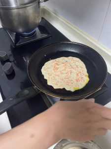 Immediately tilt the wok and use the back of the ladle to spread the batter outward into a thin, even round, working quickly before the egg sets.