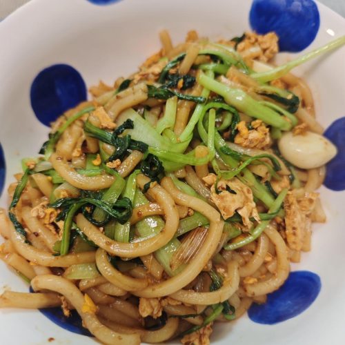 Stir-fried udon noodles with egg and greens in a wok