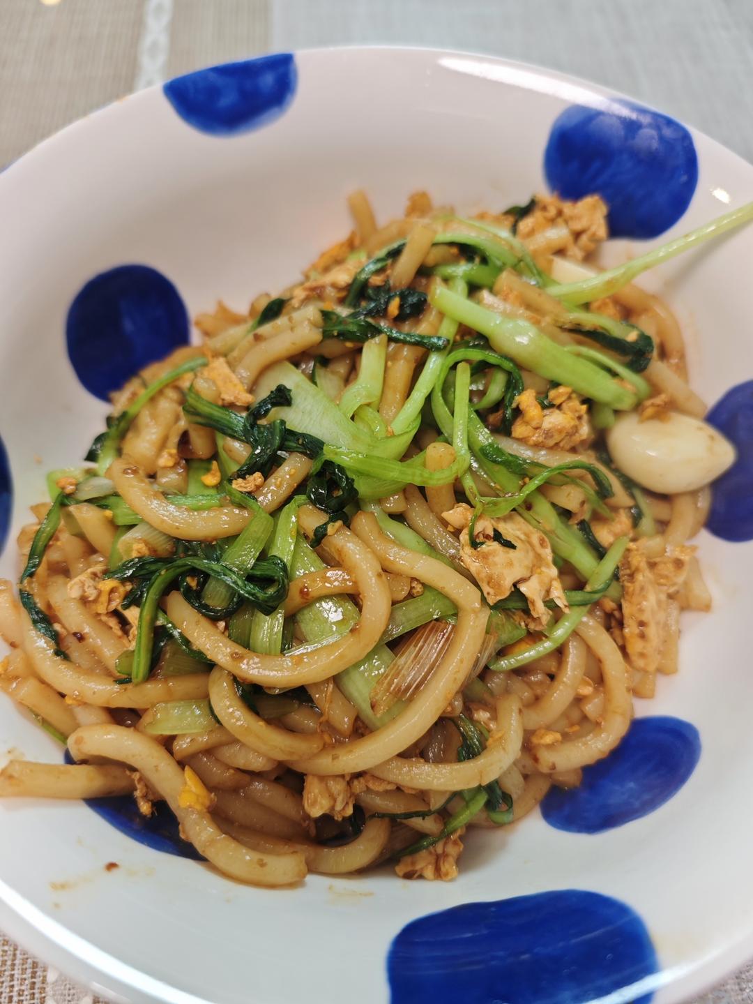 Stir-fried udon noodles with egg and greens in a wok