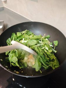 Leafy greens added to the wok with soy sauce