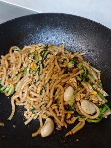 Cumin being sprinkled over the noodles in the wok