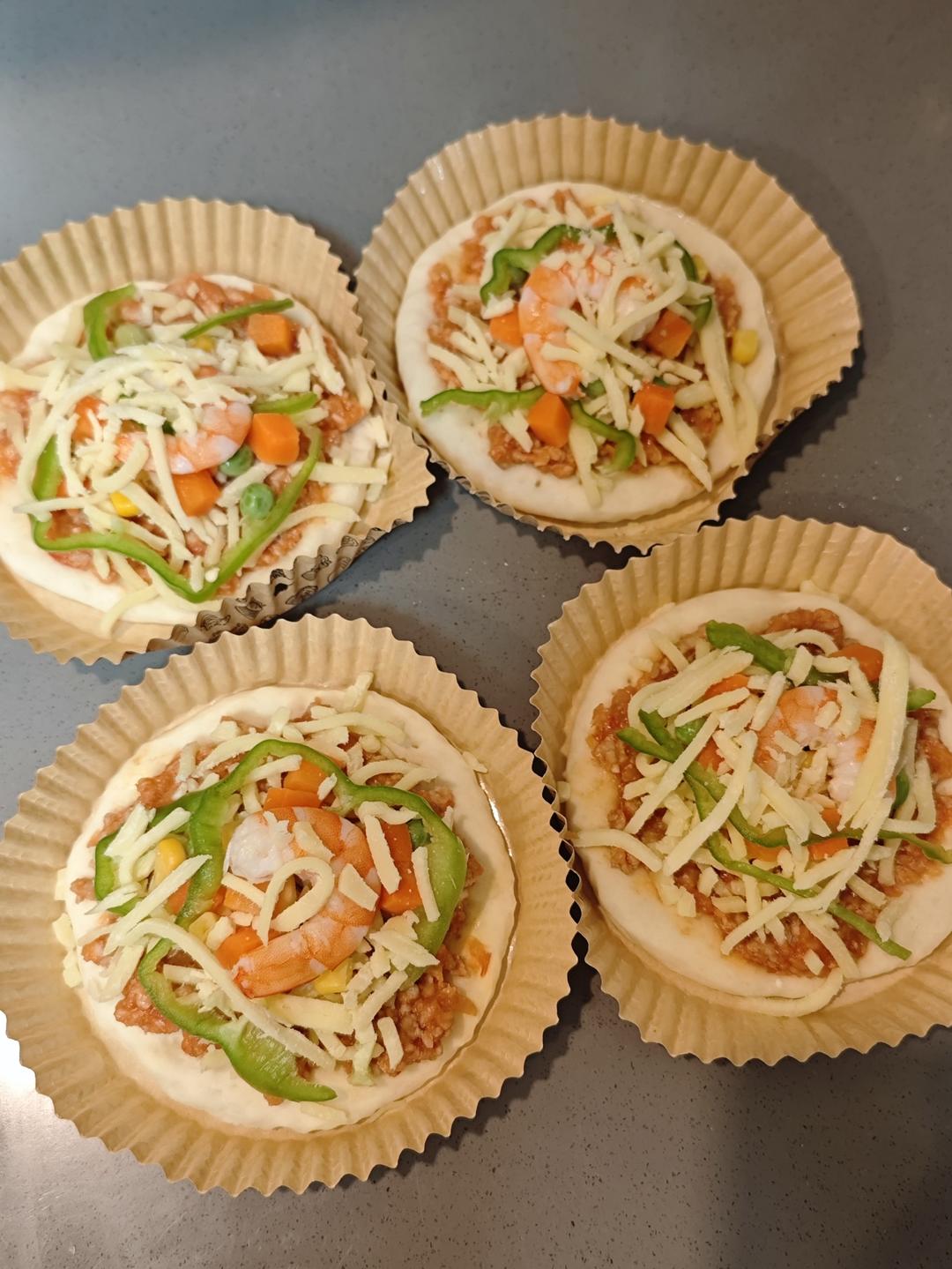 Mini pizzas assembled with sauce, toppings, and mozzarella