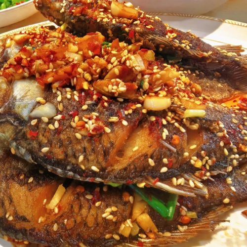 Fried crucian carp on a plate with chili, sesame, and scallion