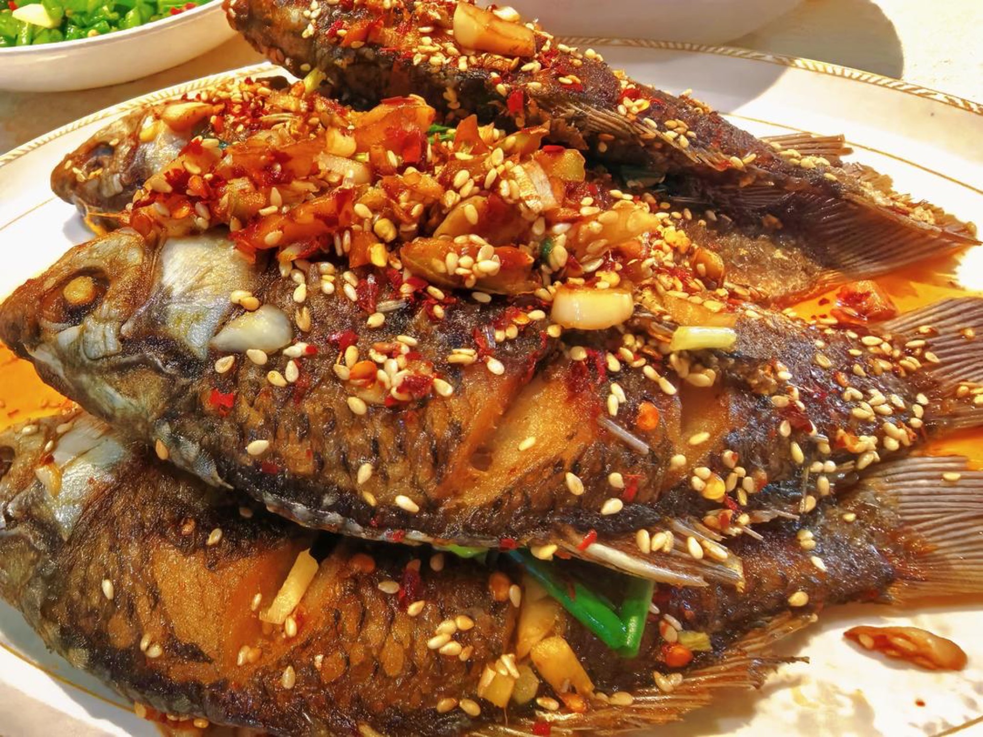 Fried crucian carp on a plate with chili, sesame, and scallion