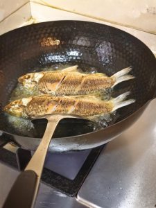 Crucian carp being flipped in hot oil in a wok