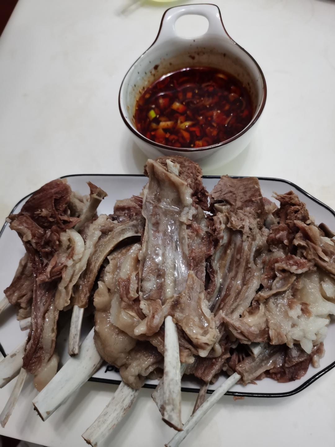 Whole boiled lamb rack on a cutting board with a bowl of chili dipping sauce