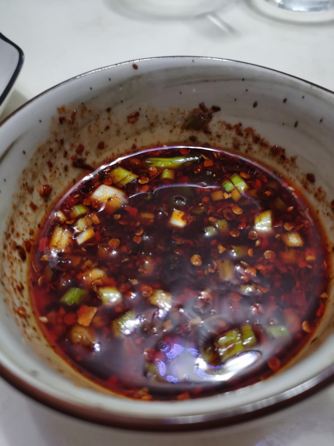 Pouring hot oil over scallion garlic and chili flakes in the dipping bowl