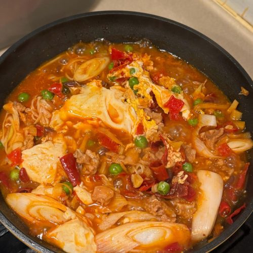 Korean spicy rabbit tofu soup in a dark pot with soft tofu, enoki mushrooms, and scallions